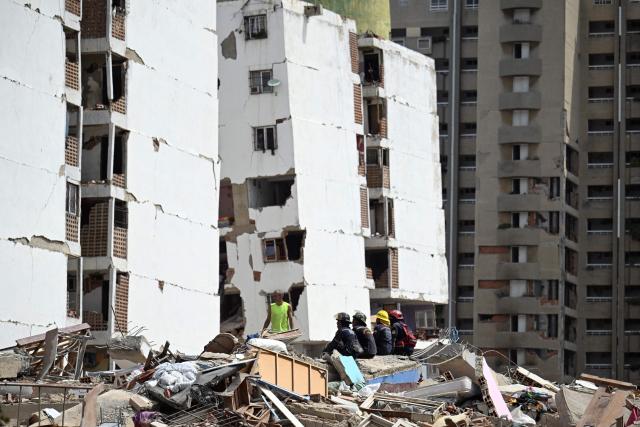 Firefighters sit on the rubble in front of heavily damaged apartment buildings following an earthquake in Catia La Mar, La Guaira state, about 30 km northwest of Caracas, on June 25, 2026. A twin earthquake that was Venezuela's largest in over a century has killed at least 164 people and destroyed multiple buildings near the capital, where residents searched on June 25 for missing relatives. (Photo by Juan BARRETO / AFP)