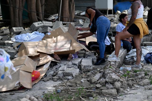 EDITORS NOTE: Graphic content / People inspect bodies covered with cardboard amid the rubble of collapsed buildings following an earthquake in Catia La Mar, La Guaira state, about 30 km northwest of Caracas, on June 25, 2026. A twin earthquake that was Venezuela's largest in over a century has killed at least 164 people and destroyed multiple buildings near the capital, where residents searched on June 25 for missing relatives. (Photo by Juan BARRETO / AFP)