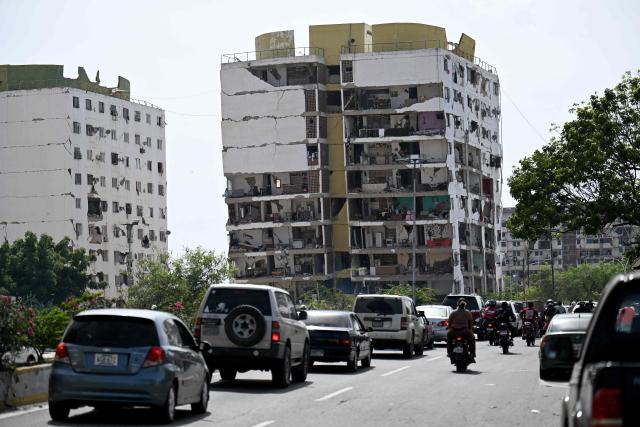 Traffic moves along a road past heavily damaged apartment buildings following an earthquake in Catia La Mar, La Guaira state, about 30 km northwest of Caracas, on June 25, 2026. A twin earthquake that was Venezuela's largest in over a century has killed at least 164 people and destroyed multiple buildings near the capital, where residents searched on June 25 for missing relatives. (Photo by Juan BARRETO / AFP)
