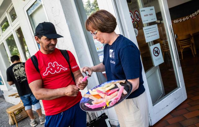 A volunteer at a community centre of the Berliner Stadt Mission (Berlin City Mission) distributes frozen popsicles to a homeless man in Berlin on June 25, 2026, as the capital braces for temperatures hovering around 40 degrees centigrade over the weekend. (Photo by John MACDOUGALL / AFP)