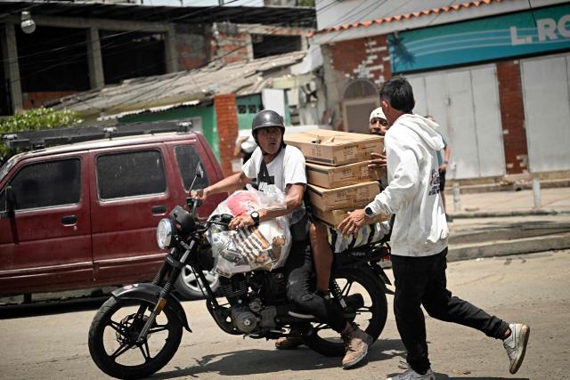 People carry goods on a motorbike as looting erupted in Catia La Mar, La Guaira State, about 30 km northwest of Caracas, on June 25, 2026, following an earthquake. A twin earthquake that was Venezuela's largest in over a century has killed at least 164 people and destroyed multiple buildings near the capital, where residents searched on June 25 for missing relatives. (Photo by Federico PARRA / AFP)