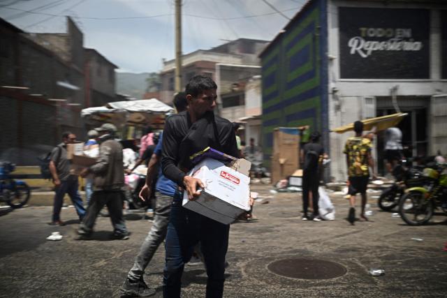 A man carries a box as looting erupted in Catia La Mar, La Guaira State, about 30 km northwest of Caracas, on June 25, 2026, following an earthquake. A twin earthquake that was Venezuela's largest in over a century has killed at least 164 people and destroyed multiple buildings near the capital, where residents searched on June 25 for missing relatives. (Photo by Federico PARRA / AFP)