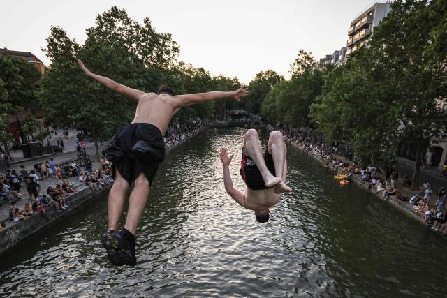 Youths jump from a bridge into the Canal Saint-Martin as France experiences a heatwave, in Paris on June 25, 2026. Due to the ongoing heatwave sweeping across France - the Bassin des Recollets - a portion of the Canal Saint-Martin in the French capital has been opened for swimming from June 17. (Photo by Ludovic MARIN / AFP)