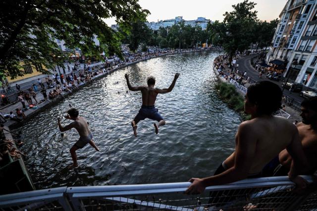 Youths jump from a bridge into the Canal Saint-Martin as France experiences a heatwave, in Paris on June 25, 2026. Due to the ongoing heatwave sweeping across France - the Bassin des Recollets - a portion of the Canal Saint-Martin in the French capital has been opened for swimming from June 17. (Photo by Ludovic MARIN / AFP)