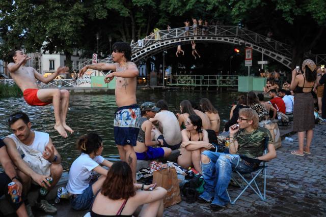 A youth jump from the crowded canal bank into the Canal Saint-Martin as France experiences a heatwave, in Paris on June 25, 2026. Due to the ongoing heatwave sweeping across France - the Bassin des Recollets - a portion of the Canal Saint-Martin in the French capital has been opened for swimming from June 17. (Photo by Ludovic MARIN / AFP)