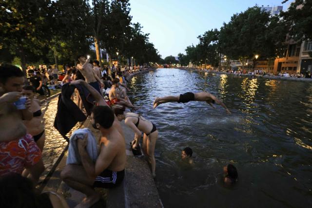 Youths cool down in the waters of the Canal Saint-Martin as France experiences a heatwave, in Paris on June 25, 2026. Due to the ongoing heatwave sweeping across France - the Bassin des Recollets - a portion of the Canal Saint-Martin in the French capital has been opened for swimming from June 17. Authorities said hospitals in Paris and its surrounding region were "saturated" and decided to ban alcohol consumption in the streets and public spaces from June 26 at noon, as well as alcohol sales from 6:00 pm. (Photo by Ludovic MARIN / AFP)