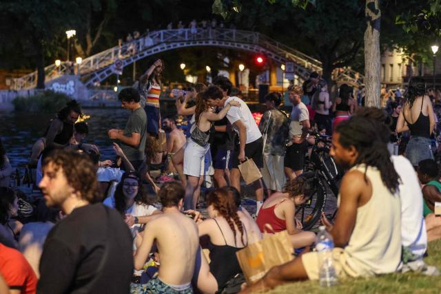 Youths sit along the Canal Saint-Martin as France experiences a heatwave, in Paris on June 25, 2026. Due to the ongoing heatwave sweeping across France - the Bassin des Recollets - a portion of the Canal Saint-Martin in the French capital has been opened for swimming from June 17. Authorities said hospitals in Paris and its surrounding region were "saturated" and decided to ban alcohol consumption in the streets and public spaces from June 26 at noon, as well as alcohol sales from 6:00 pm. (Photo by Ludovic MARIN / AFP)