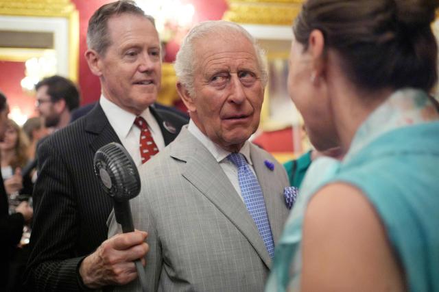 (FILES) Vice Admiral Tony Johnstone-Burt, Master of the Household to the Sovereign holds a small battery powered fan for Britain's King Charles III (C) as he attends a London Climate Week reception, hosted by the Department for Energy Security and Net Zero (DESNZ) at St James's Palace in London on June 24, 2026. Britain's King Charles III is expected to reveal his personal tax bill in a bid to improve transparency on June 25, 2026, as royal finances come under increasing public scrutiny in Britain. (Photo by Yui Mok / POOL / AFP)
