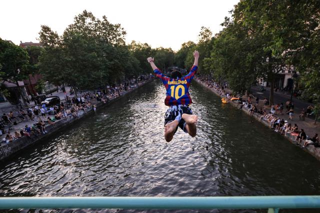 A youth jumps from a bridge into the Canal Saint-Martin as France experiences a heatwave, in Paris on June 25, 2026. Due to the ongoing heatwave sweeping across France - the Bassin des Recollets - a portion of the Canal Saint-Martin in the French capital has been opened for swimming from June 17. Authorities said hospitals in Paris and its surrounding region were "saturated" and decided to ban alcohol consumption in the streets and public spaces from June 26 at noon, as well as alcohol sales from 6:00 pm. (Photo by Ludovic MARIN / AFP)