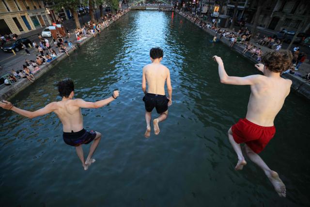 Youths jump from a bridge into the Canal Saint-Martin as France experiences a heatwave, in Paris on June 25, 2026. Due to the ongoing heatwave sweeping across France - the Bassin des Recollets - a portion of the Canal Saint-Martin in the French capital has been opened for swimming from June 17. Authorities said hospitals in Paris and its surrounding region were "saturated" and decided to ban alcohol consumption in the streets and public spaces from June 26 at noon, as well as alcohol sales from 6:00 pm. (Photo by Ludovic MARIN / AFP)