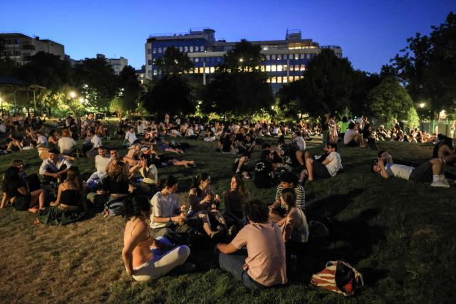 City-dwellers take to a public park to cool down at nightfall, along the Canal Saint-Martin as France experiences a heatwave, in Paris on June 25, 2026. Due to the ongoing heatwave sweeping across France - the Bassin des Recollets - a portion of the Canal Saint-Martin in the French capital has been opened for swimming from June 17. Authorities said hospitals in Paris and its surrounding region were "saturated" and decided to ban alcohol consumption in the streets and public spaces from June 26 at noon, as well as alcohol sales from 6:00 pm. (Photo by Ludovic MARIN / AFP)