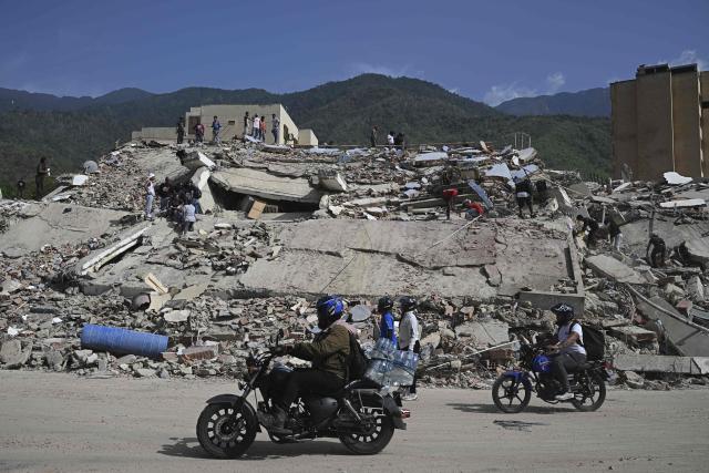 Locals ride past a collapsed building where volunteers are searching for possible victims amid the rubble following a twin earthquake, in Caraballeda, La Guaira state, about 40 km northeast of Caracas, on June 25, 2026. The death toll from twin quakes, measured at magnitudes 7.2 and 7.5, has risen to at least 188, with more than 1,520 others injured, top lawmaker Jorge Rodriguez reported, while residents continue searching for missing relatives. (Photo by Federico PARRA / AFP)