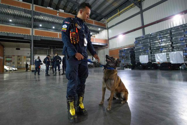 A Colombian firefighter with a search-and-rescue dog stands inside a hangar at Catam Air Base in Bogota on June 25, 2026, before departing with humanitarian aid to Venezuela following deadly earthquakes. Desperate Venezuelans raced to find and rescue loved ones trapped alive beneath the rubble of collapsed buildings after two major earthquakes, measured at magnitudes 7.2 and 7.5, hit northern Venezuela killing at least 235 people and leaving more than 1,500 injured. (Photo by Sebastian BARROS / AFP)