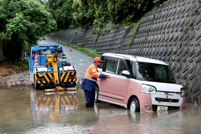 A tow lorry driver retrieves a partially submerged car after flooding in the town of Kashiwara, Osaka prefecture on June 26, 2026. Japanese airlines cancelled more than 100 flights on june 26, as two tropical storms barrelled towards the archipelago, with authorities advising evacuations in some areas because of possible flooding and landslides. (Photo by PAUL MILLER / AFP)
