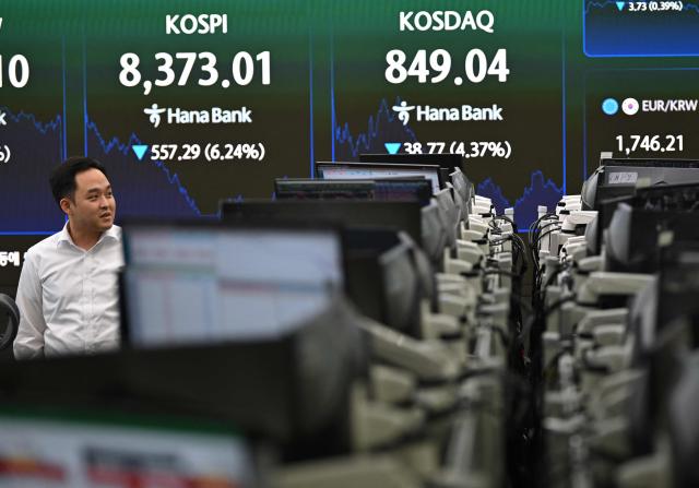 A currency dealer walks past an electronic screen showing South Korea's benchmark stock index (KOSPI) in a foreign exchange dealing room at the Hana Bank headquarters in Seoul on June 26, 2026. South Korean stocks collapsed more than eight percent on June 26, sparking a 20 minute halt in trading, amid a fresh rout in tech firms and following a sell-off on Wall Street. (Photo by Jung Yeon-je / AFP)