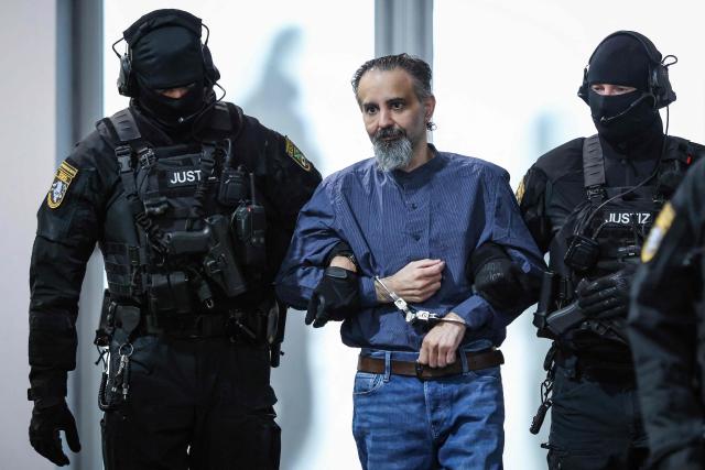 Judicial officers escort Saudi Arabian defendant Taleb Al Abdulmohsen (C) to the courtroom upon his arrival on June 26, 2026 in Magdeburg, eastern Germany, before his trial for driving an SUV through a crowd at a Christmas market. The court sentenced to life in jail the Saudi psychiatrist who drove an SUV through a crowded Christmas market in 2024, killing six people and injuring more than 300. (Photo by Ronny HARTMANN / AFP)