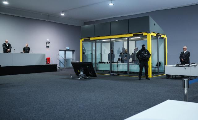 Saudi Arabian defendant Taleb Jawad al-Abdulmohsen (C) stands next to an judicial security officer as he waits inside a bulletproof glass box in the temporary courtroom in Magdeburg, eastern Germany, before his trial for driving an SUV through a crowd at a Christmas market. The court sentenced to life in jail the Saudi psychiatrist who drove an SUV through a crowded Christmas market in 2024, killing six people and injuring more than 300. (Photo by Ronny HARTMANN / AFP)