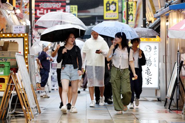 People use umbrellas to shelter from the rain on a street in Osaka on June 26, 2026. Japanese airlines cancelled more than 100 flights on june 26, as two tropical storms barrelled towards the archipelago, with authorities advising evacuations in some areas because of possible flooding and landslides. (Photo by PAUL MILLER / AFP)
