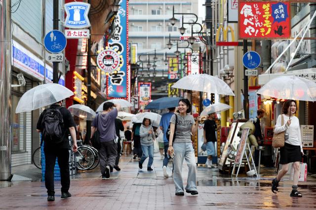 People use umbrellas to shelter from the rain on a street in Osaka on June 26, 2026. Japanese airlines cancelled more than 100 flights on june 26, as two tropical storms barrelled towards the archipelago, with authorities advising evacuations in some areas because of possible flooding and landslides. (Photo by PAUL MILLER / AFP)