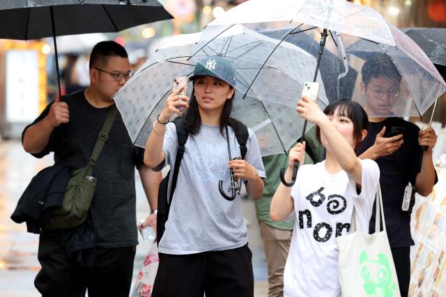 People use umbrellas to shelter from the rain on a street in Osaka on June 26, 2026. Japanese airlines cancelled more than 100 flights on june 26, as two tropical storms barrelled towards the archipelago, with authorities advising evacuations in some areas because of possible flooding and landslides. (Photo by PAUL MILLER / AFP)