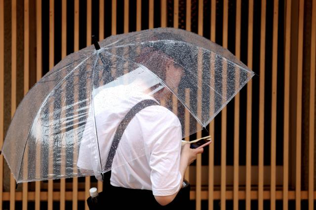 A tourist uses an umbrella to shelter from the rain in Osaka on June 26, 2026. Japanese airlines cancelled more than 100 flights on june 26, as two tropical storms barrelled towards the archipelago, with authorities advising evacuations in some areas because of possible flooding and landslides. (Photo by PAUL MILLER / AFP)