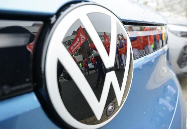(FILES) Employees of Volkswagen (VW) are reflected in the logo of a VW car as they demonstrate in front of the plant of German car maker Volkswagen (VW), on December 2, 2024 in Zwickau, eastern Germany, as thousands of Volkswagen workers go on strike all over Germany in an escalating industrial dispute at the crisis-hit German auto giant with thousands of jobs at stake. According to a media report on June 26, 2026, the car manufacturer Volkswagen plans to cut up to 100,000 jobs. Four plants in Germany are to be closed, the "Manager Magazin" reported, citing insiders. In addition, VW CEO Oliver Blume is reportedly planning to spin off the core Volkswagen brand into a new company. According to the report, the job cuts are planned worldwide. (Photo by Jens Schlueter / AFP)