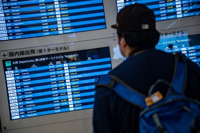 Screens show delayed flights in the departure hall of Tokyo's Haneda Airport on June 26, 2026. Japanese airlines cancelled more than 100 flights on June 26 as two tropical storms barrelled towards the archipelago, with authorities advising evacuations in some areas because of possible flooding and landslides. (Photo by Philip FONG / AFP)