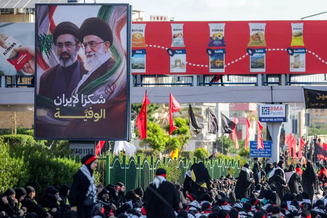 A billboard depicting Iran's late and current supreme leaders Ali Khamenei and his son Mojtaba Khamenei is displayed as Shia Muslim devotees gather for a mourning procession in Beirut’s southern suburbs on June 26, 2026 at the peak of Ashura, a 10-day period commemorating the seventh century killing of Prophet Mohammed's grandson Imam Hussein. (Photo by ibrahim AMRO / AFP)