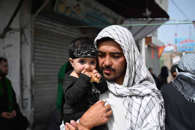 An Afghan Shiite Muslim carries his child along a road, on the tenth day of Ashura during the Islamic holy month of Muharram in Kandahar on June 26, 2026. (Photo by Sanaullah SEIAM / AFP)