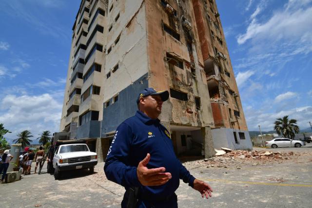 A police officer stands next to damaged building in Moron, state of Carabobo, Venezuela, on June 26, 2026, following deadly earthquakes. Using heavy equipment or their bare hands, rescuers and volunteers searched for survivors of the twin earthquake in Venezuela, which has officially left 589 dead and, according to estimates, thousands missing. (Photo by Orlando Obispo / AFP)