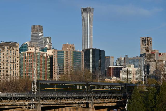 (FILES) A train passes before buildings including the CITIC Tower (top C) in Beijing on December 3, 2024. An eyewitness reported plane debris at the base of Beijing's tallest building on June 26, 2026, which AFP journalists saw had a large hole torn into the upper floors as police cordoned off the area. Video footage taken from a nearby building by the witness showed fire trucks blasting water at smoke billowing from the 528-metre (1,732-foot) CITIC Tower, while the wreck of a plane lay on the ground beside the building. (Photo by ADEK BERRY / AFP)
