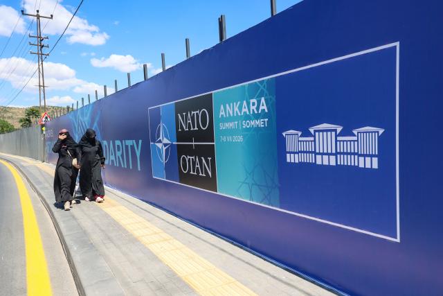 Local residents walk past  billboards with the slogans “Key to Peace,” “Key to Security,” and “Shared Future in Peace”, displayed along the boulevard on the protocol route ahead of the NATO Summit in Ankara, on 26 June 2026. The 36th NATO summit will be held in Ankara on July 7-8, 2026. (Photo by ADEM ALTAN / AFP)