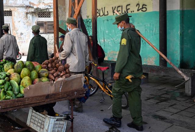 Cuban soldiers walk past a street fruit stall while heading to clear rubbish from street-corner dumps caused by the breakdown of waste collection amid the country’s ongoing crisis, in Old Havana, Cuba, on June 26, 2026. (Photo by YAMIL LAGE / AFP)