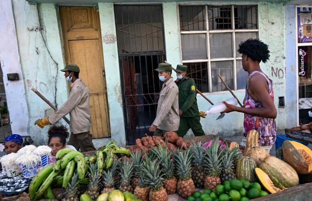 Cuban soldiers walk past a street fruit stall while heading to clear rubbish from street-corner dumps caused by the breakdown of waste collection amid the country’s ongoing crisis, in Old Havana, Cuba, on June 26, 2026. (Photo by YAMIL LAGE / AFP)