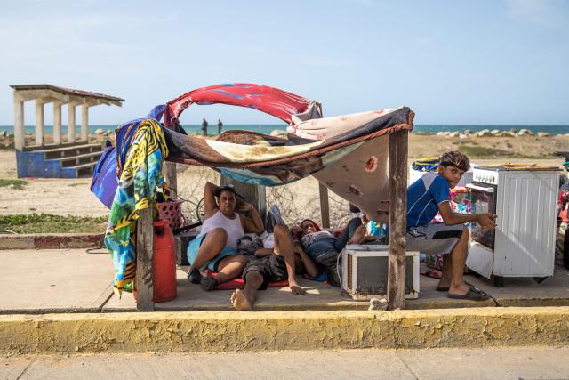 People remain under a makeshift shelter on the sidewalk by the beach following twin earthquakes in Caraballeda, La Guaira State, some 40 km northeast of Caracas, on June 25, 2026. The death toll from twin earthquakes in Venezuela more than doubled on June 26, 2026, to 589, interim president Delcy Rodriguez said, as rescuers boosted by international teams raced to find survivors beneath collapsed buildings. Over 50,000 people are missing after the earthquakes in Venezuela, a senior UN official told AFP. (Photo by Donaldo BARROS / AFP)