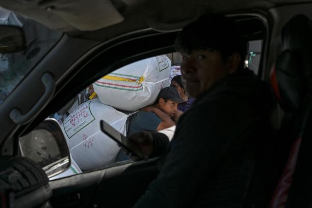 A worker carries a sack of coca leaves as another person sits inside a vehicle at the legal coca market in La Paz, on June 26, 2026. (Photo by MARTIN BERNETTI / AFP)