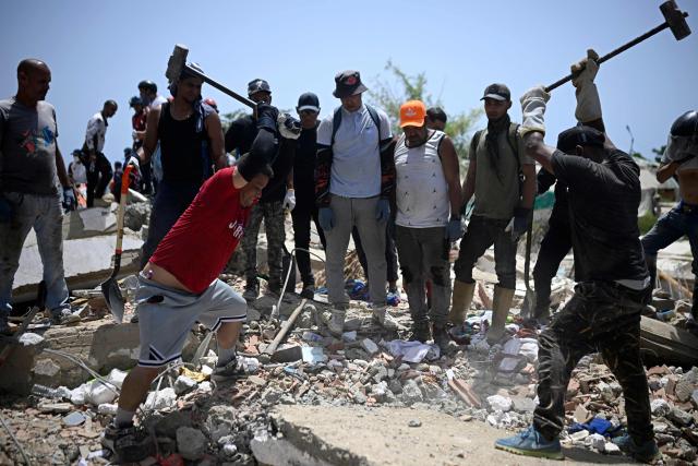 Men use sledgehammers to break through concrete on the rubble of collapsed buildings in Catia La Mar, La Guaira, Venezuela, on June 26, 2026, following deadly earthquakes. The death toll from two powerful earthquakes that devastated Venezuela earlier this week rose to 920 on June 26, National Assembly President Jorge Rodriguez said. (Photo by Federico PARRA / AFP)