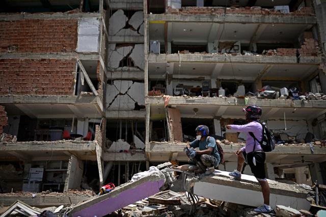 People stand on rubble in front of a damaged multi-storey building in Catia La Mar, La Guaira, Venezuela, on June 26, 2026, following earthquakes. The death toll from two powerful earthquakes that devastated Venezuela earlier this week rose to 920 on June 26, National Assembly President Jorge Rodriguez said. (Photo by Federico PARRA / AFP)