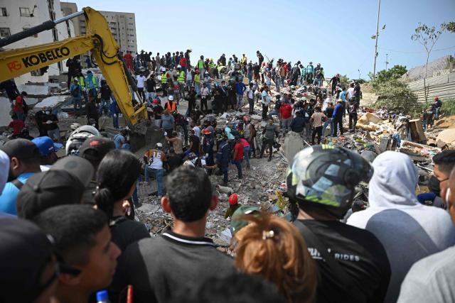 EDITORS NOTE: Graphic content / Rescuers, volunteers and residents gather around an excavator as they search through the rubble of collapsed buildings in Catia La Mar, La Guaira, Venezuela, on June 26, 2026, following deadly earthquakes. The death toll from two powerful earthquakes that devastated Venezuela earlier this week rose to 920 on June 26, National Assembly President Jorge Rodriguez said. (Photo by Federico PARRA / AFP)
