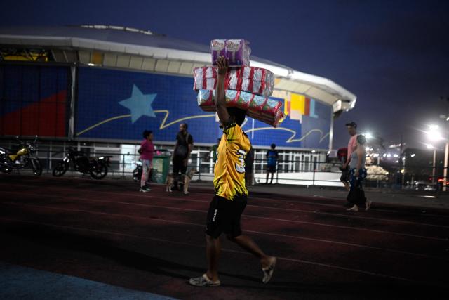 A man carries boxes of donated supplies at the Jose Maria Vargas sports complex in Maiquetia, Vargas State, Venezuela, on June 26, 2026, following deadly earthquakes that struck the country. The death toll from two powerful earthquakes that devastated Venezuela earlier this week rose to 920 on June 26, National Assembly President Jorge Rodriguez said. (Photo by Federico PARRA / AFP)