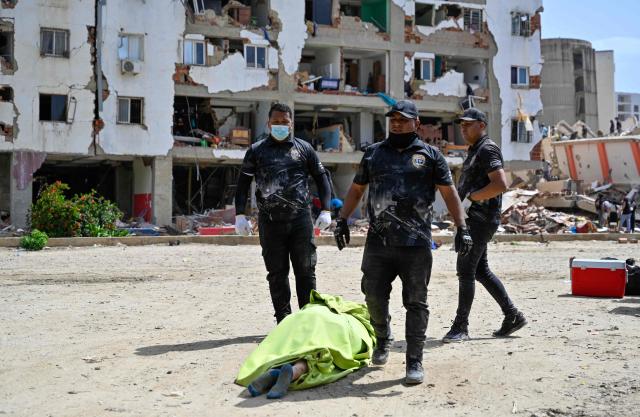 EDITORS NOTE: Graphic content / Members of the Venezuelan forensic police stand next to a body covered with a green sheet at the site of collapsed buildings following earthquakes in Caraballeda, La Guaira state, Venezuela, on June 26, 2026. The death toll from two powerful earthquakes that devastated Venezuela earlier this week rose to 920 on June 26, National Assembly President Jorge Rodriguez said. (Photo by Maryorin Mendez / AFP)