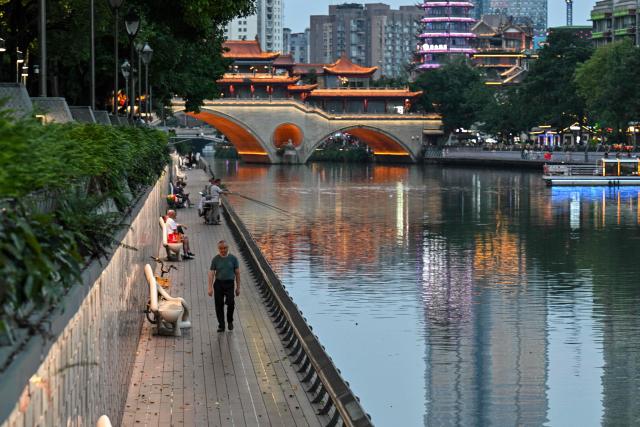 People walk along the Jin River in Chengdu, in China's southwestern Sichuan province on June 26, 2026. (Photo by HECTOR RETAMAL / AFP)