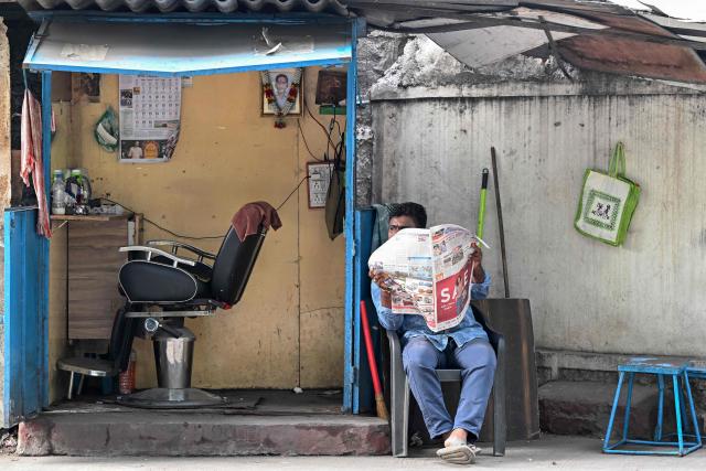 A roadside barber reads a newspaper as he waits for customers in Hyderabad on June 27, 2026. (Photo by Noah SEELAM / AFP)
