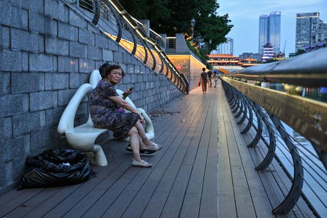 People sit on a bench along the Jin River in Chengdu, in China's southwestern Sichuan province on June 26, 2026. (Photo by HECTOR RETAMAL / AFP)