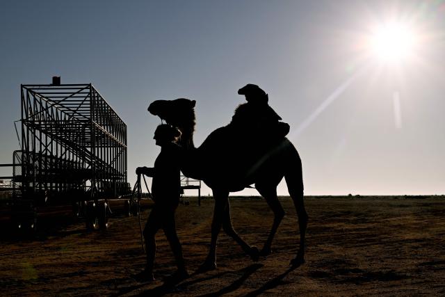 Trainer Kyrraley Woodhouse (L) leads a camel to the track with her five-year-old son Clancy onboard for the Marree Australasian Camel Cup run in the South Australian outback town of Marree on June 27, 2026. The Camel Cup is a much-loved outback event celebrating camel racing, Afghan cameleer heritage, community and culture. Camels were instrumental in helping settlers open the outback of Australia to development until trains took over. (Photo by William WEST / AFP)