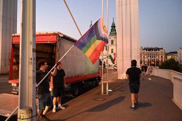 Local workers replace 'Progress Pride' rainbow flags on the Erzsebet Bridge in Budapest, Hungary, on June 26, 2026, a day before Budapest Pride. A right-wing sympathizer removed several flags and threw them into the Danube, after which activists from far-right parliamentary party, the 'Our Homeland Movement' placed Hungarian national flags on the bridge few days ago. (Photo by Attila KISBENEDEK / AFP)