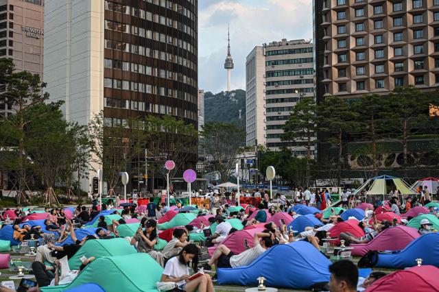People sit on bean bags as the Seoul Tower is seen in the background at a plaza in Seoul on June 27, 2026. (Photo by Jade GAO / AFP)