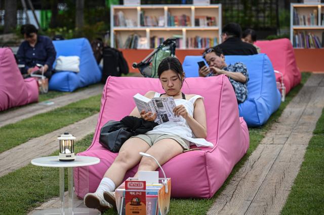 A woman sitting on a bean bag reads a book at a plaza in Seoul on June 27, 2026. (Photo by Jade GAO / AFP)
