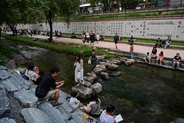 People walk across stepping stones in the Cheonggyecheon Stream in Seoul on June 27, 2026. (Photo by Jade GAO / AFP)