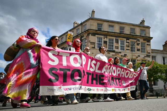 EDITORS NOTE: Graphic content / British political activist and lawyer Aamer Anwar (C) and protesters display a banner as they take part in an anti-racism "Unity March and Rally", organised by Stand up to Racism, Scotland in Edinburgh on June 27, 2026. (Photo by ANDY BUCHANAN / AFP)
